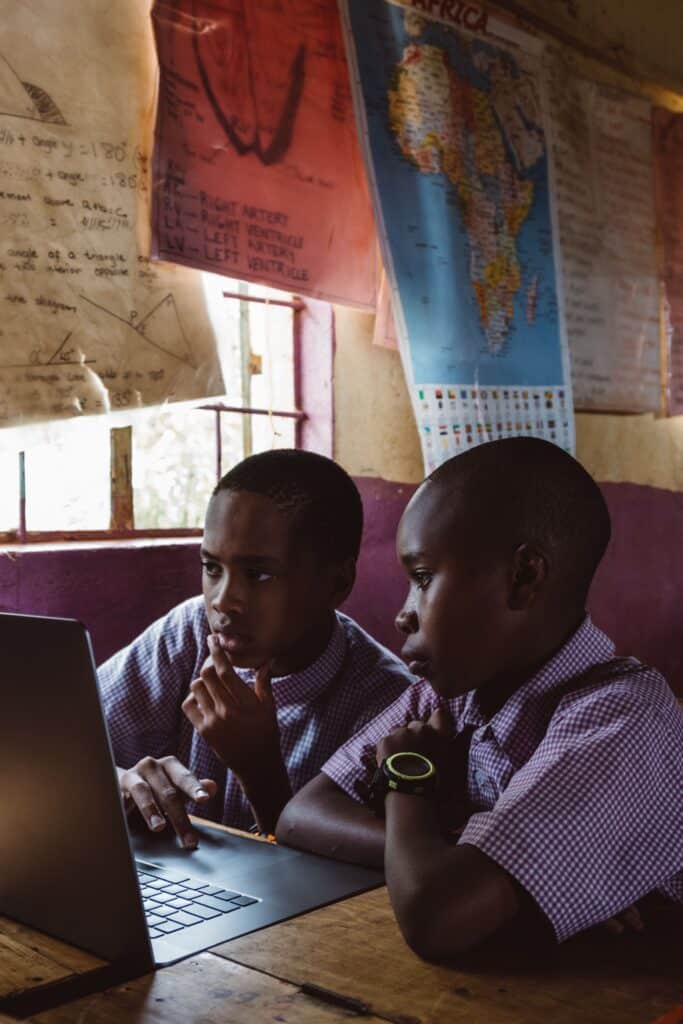 What effective school leadership looks like across Africa Two boys in school uniforms learning together on a laptop indoors with educational posters in the background.