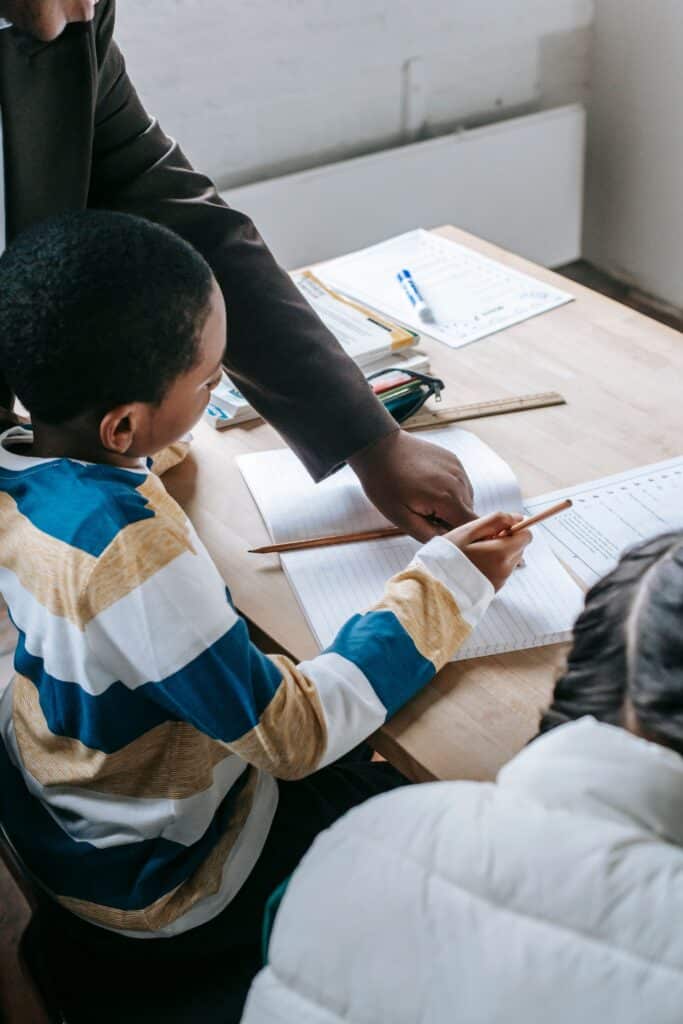 Crop black female helping ethnic boy and girl with assignment while studying in school classroom