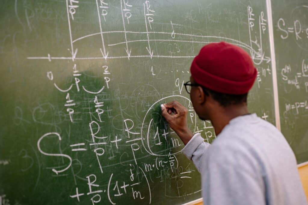 Factors shaping ICT uptake in education sector Student writing complex mathematical equations on a chalkboard in a classroom setting.
