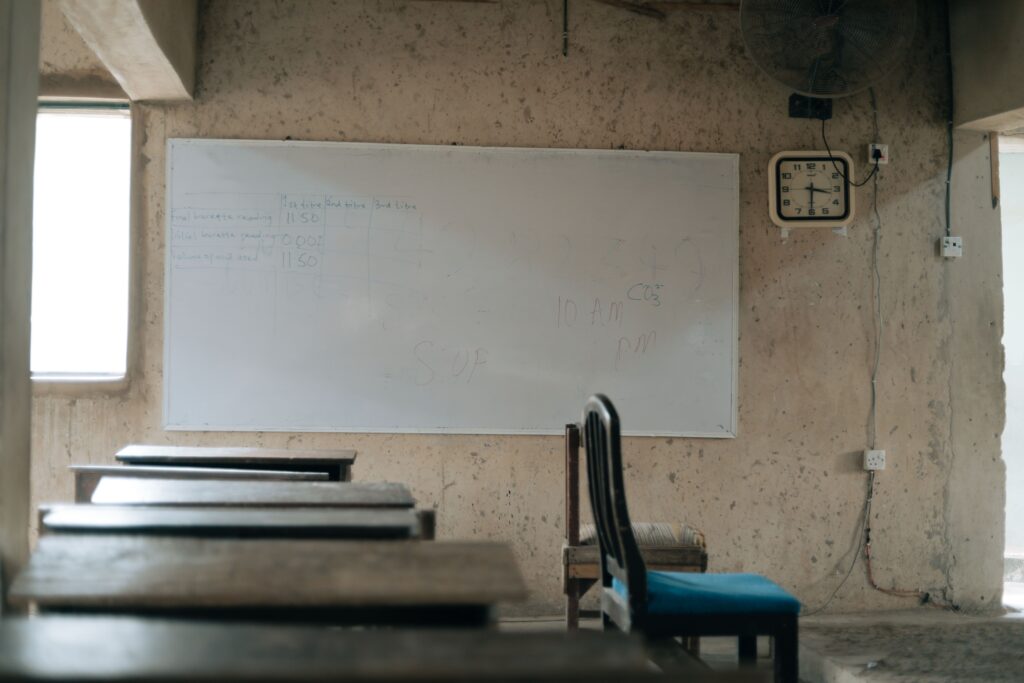 What school leaders in Nigeria and South Africa need for Education 4.0 An empty classroom featuring old wooden desks, a whiteboard, and a wall clock, highlighting education.
